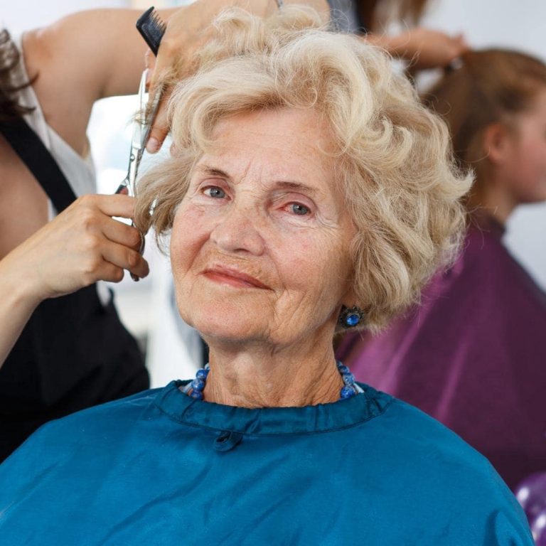 Photo of older woman with light curly hair getting a hair cut